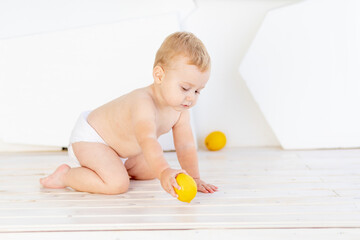Obraz na płótnie Canvas a small child a boy six months old plays on the floor in a bright white room in diapers with lemons and oranges