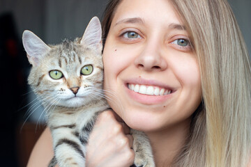A young beautiful blonde woman without makeup with a beautiful smile, dimples near Tabby kitten with green eyes. Good friends. Friendship of a pet and its owner