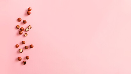 Cracked macadamia nuts on pink background with copy space