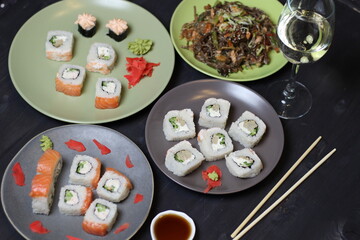 Safood buckwheat noodles stuffes with cucumber and sesame in green plate, rice rolls, white wine glass on black table with chopsticks and soy sauce