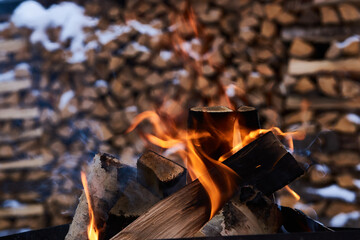 Burning firewood with stacked firewood on background