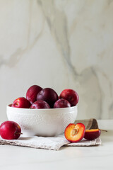 Ripe red plums in a white plate on marble background. Healthy food. 