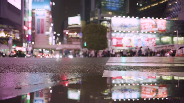 Low angle shots of people at Shibuya Crossing square on a rainy night. Showing shoppers and night life in the neon city. Tokyo, Japan.