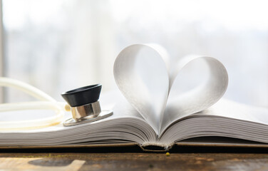 An open book. The pages are folded in the shape of a heart. A stethoscope pressed against the...