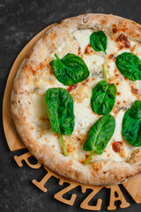 Homemade pizza with four cheeses, gorgonzola, parmesan, camembert, emmental and spinach on a dark background. Top view, side view