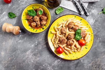 penne pasta with meatballs and tomato sauce on a yellow plate and a gray background, italian pasta