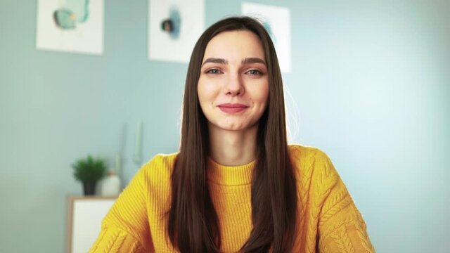 Young happy woman in yellow sweater is smiling and chatting on webcam with her followers. Female blogger makes live stream by video call with viewers. Remote communication. Social network and Internet