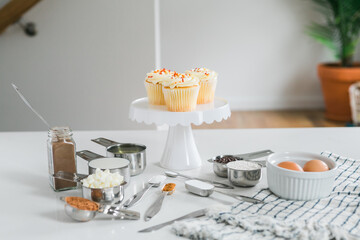 Vanilla cupcakes on stand in kitchen surrounded by ingredients and measuring spoons