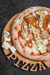 Homemade vegetarian pizza with grilled vegetables. Tomato sauce, bell pepper, eggplant, zucchini, mozzarella and cheese on a dark background. Top view, side view