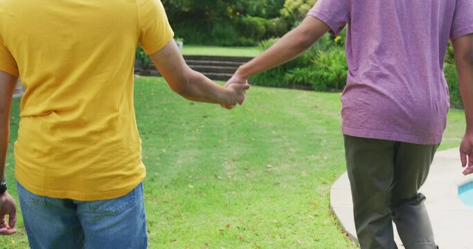 Midsection of mixed race gay male couple holding hands walking in garden