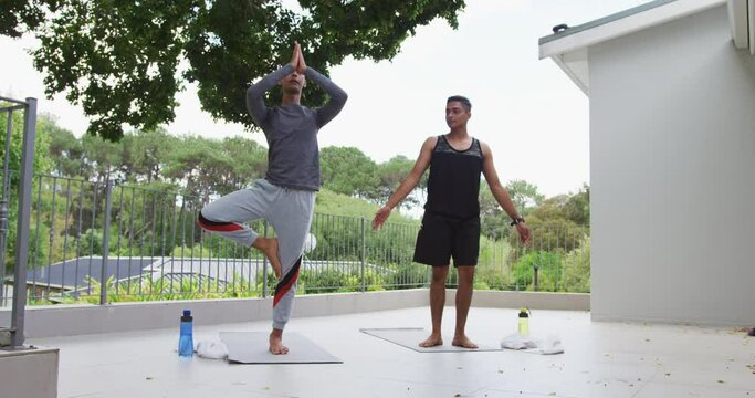 Mixed race gay male couple standing on terrace practicing yoga