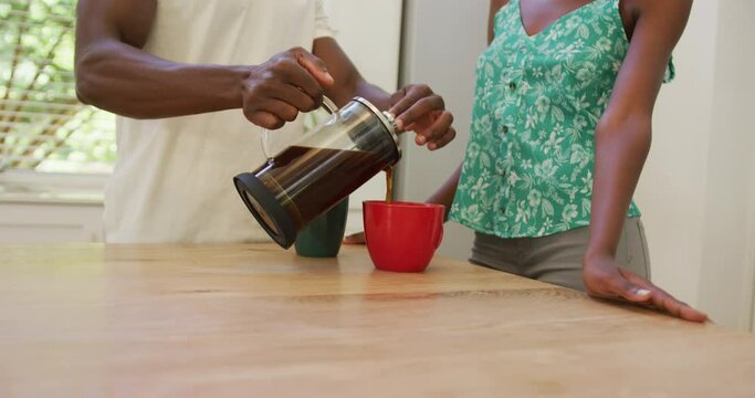 Midsection of african american couple in kitchen pouring coffee from cafetiere