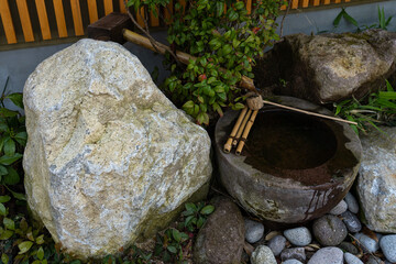 Bamboo water spout fountain on rock basin next to natural stones , water running by ladle ,this is traditional Japanese Zen Garden in Japan.