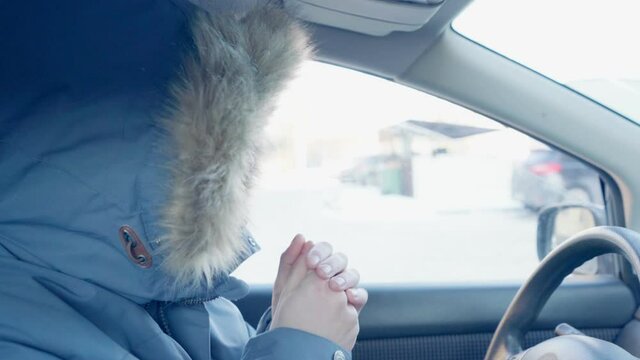 man in a winter jacket is sitting in a car. a man warms up a car in the cold. severe frost