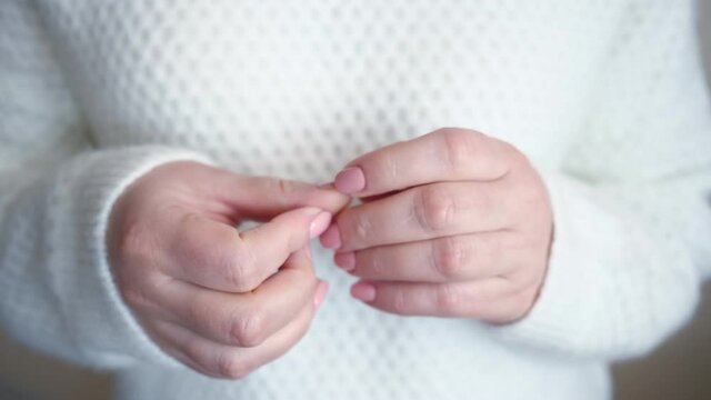 Young woman in white sweater scratches agnails on fingers suffering from emotional disorder on blurred background extreme close crop view