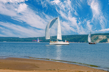 Sailing yachts sail under a beautiful blue sky with cirrus clouds, the reflection of the sun in the...