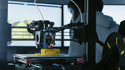 3d Printer printing yellow small house with engineer constructor in background at pc model