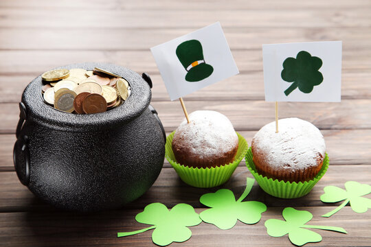 Pot of coins, cupcakes and flags with picture of St. Patrick's hat and clover leaf on dark brown wooden background