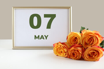 day of the month 07 May calendar photo frame and yellow rose on a white table