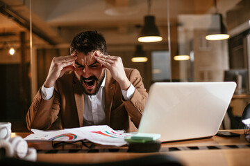Young businessman working with laptop at office. Tired man sitting at office desk working on laptop computer