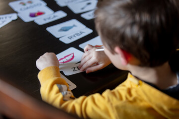 little boy learns words from cards under the ABA therapy program at home at the table