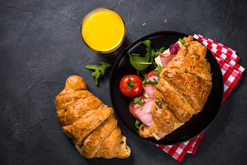 Croissant sandwich with ham, cheese and vegetables at black stone table. Top view with copy space.