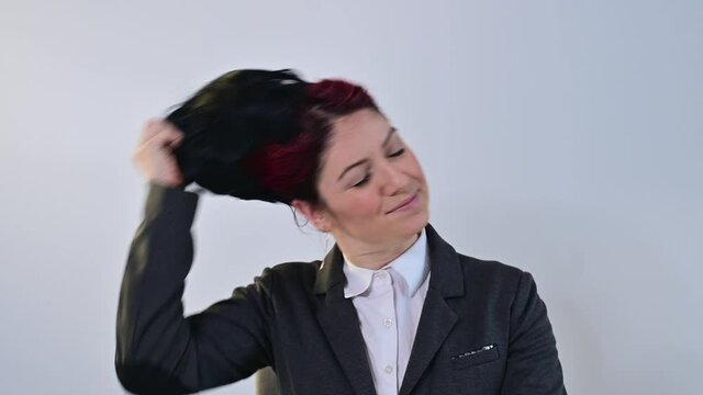 Caucasian woman in suit takes off glasses and wig on white background.
