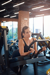 Portrait of a serious sportswoman in black clothing which poses on training apparatus looking at camera in health's club gymnastic hall.