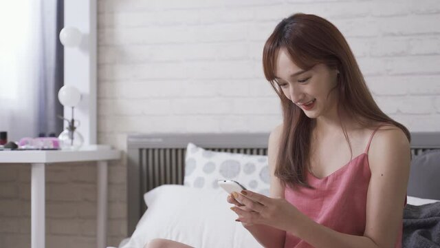 closeup korean female in pajamas is having fun playing mobile games in leisure. cheerful young lady phubbing on relaxing sunday morning. technology and indoor recreation