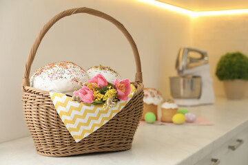 Traditional Easter cakes and flowers in basket on kitchen counter, space for text