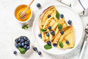Crepes with blueberries and honey in white plate at white stone table. Top view with copy space.