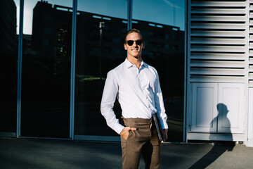 Half length portrait of cheerful male manager posing at metropolitan urban setting waiting colleague for business meeting in downtown, successful Caucasian director smiling at camera during work break