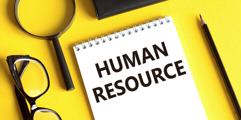 Notepad with the text HUMAN RESOUCE on a yellow background with glasses, a magnifying glass and a pencil. Business concept.