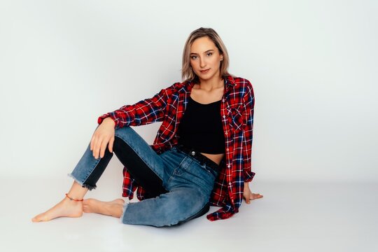 Young beautiful woman 20 years old wearing trendy black t-shirt, blue jeans and red check shirt. sexy female posing isolated near white wall in studio. 