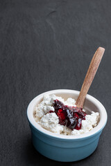 Cottage cheese with blueberry jam in ceramic bowl on black stone background