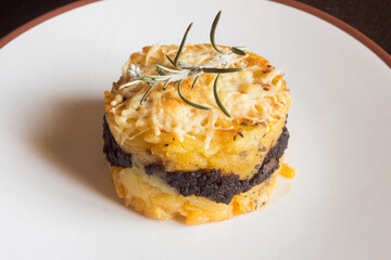 A fresh branch of rosemary on a potato tart with chocolate black pudding and gratin cheese in a...