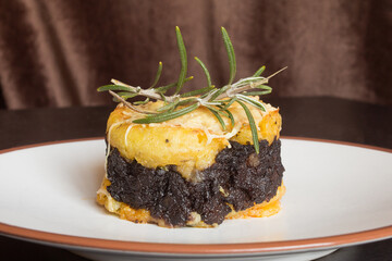 Close-up of a butter potato cake with black pudding cream with chocolate, grated cheese, and a...