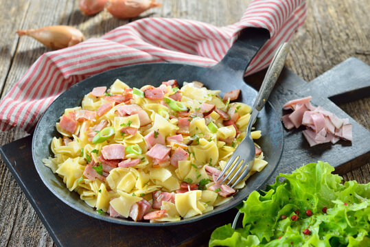 Deftige &ouml;sterreichische K&uuml;che: Schinkenfleckerl in der Eisenpfanne serviert, dazu ein kleiner Blattsalat - Austrian cuisine: Special ham pasta in an iron frying pan served with a green side salad 