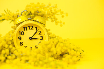 Spring mimosa flowers with a yellow alarm clock on a yellow background. spring concept. Time-spring