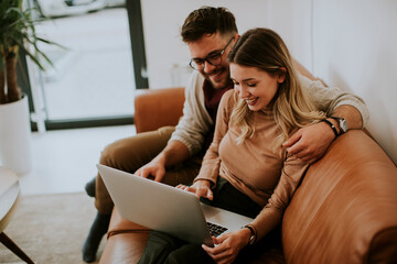 Young couple using laptop together while sitting on sofa at home