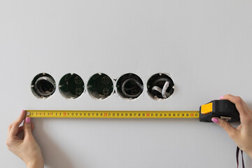 Female hands measure the length of the wall with a tape measure