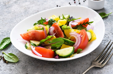 Mix salad with peppers, tomatoes and cucumber in a plate on a concrete background. Ala Greek salad.