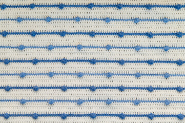 Crochet product from multicolored threads. Handmade backdrop. Flat lay. Fragment of a plaid of blue and ivory tone. Striped, geometric pattern.