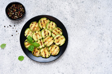 Young, juicy grilled zucchini with sauce in a black plate on a concrete background.