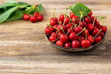 Ripe sweet cherries with green leaves in a metal plate on wooden background