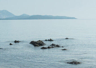 Fototapeta premium small rocks in the sea, beach view at dawn with hills on the horizon. Coasts of sardegna at dawn , olbia.