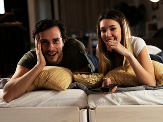 Fototapeta premium Young loving couple relaxing on bed together. Happy couple watching movie at home.