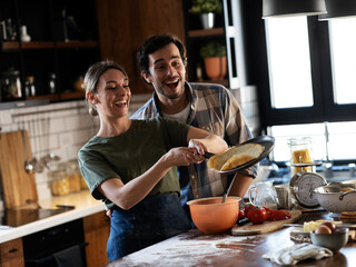 Husband and wife making pancakes at home. Young couple having fun in the kitchen.