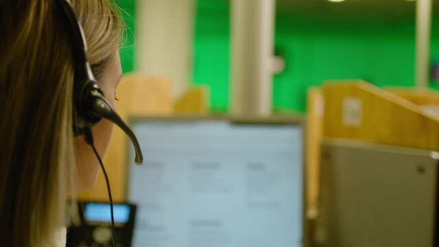 Rear view female Call centre worker in headset talking on phone and answering of questions Slow motion . Service phone operator in earphones helping customers in business office . Blurred background