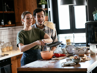 Husband and wife making pancakes at home. Young couple having fun in the kitchen.